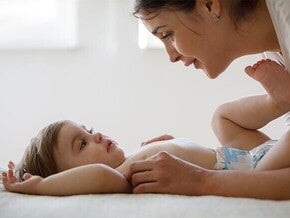 Foto: moeder kijkt liefdevol naar baby op bed, rustige warme sfeer