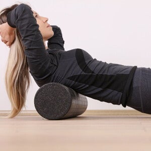 Vrouw masseert haar rug met een foamroller tijdens postpartumoefeningen