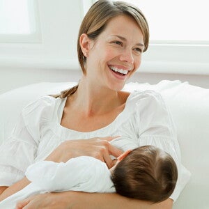 Moeder die haar baby borstvoeding geeft en glimlacht, zittend op een witte ban