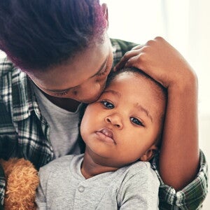 Moeder troost haar baby en geeft een kus op het hoofd, symbool van zorg en geb