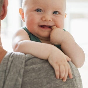 Lachende baby die op de schouder van een ouder rust en op zijn vinger bijt.