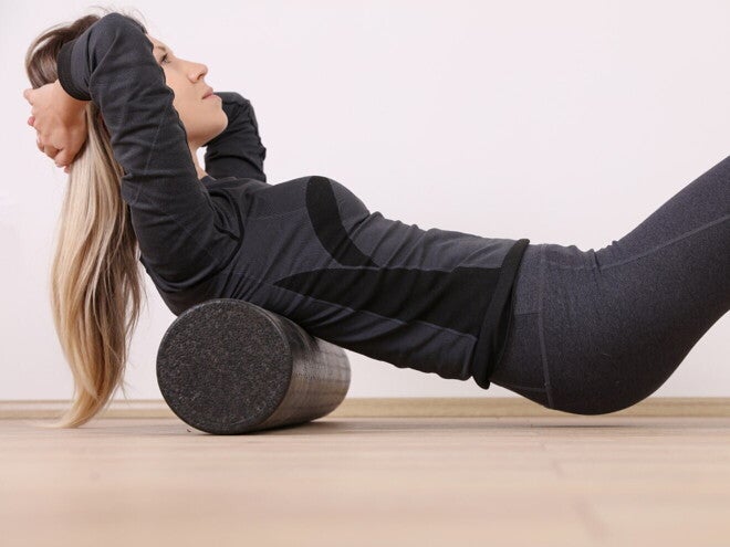 Vrouw masseert haar rug met een foamroller tijdens postpartumoefeningen