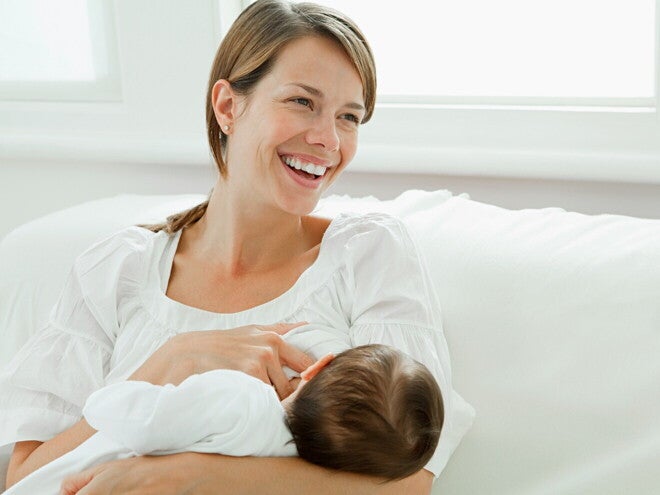 Moeder die haar baby borstvoeding geeft en glimlacht, zittend op een witte ban