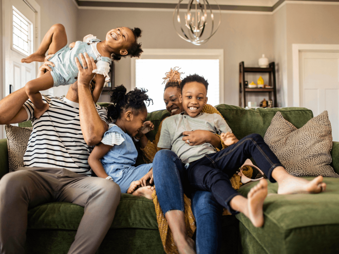 Een blije familie die samen op een bank zit te lachen, wat de ondersteuning van Nestlé FamilyNes voor ouders laat zien.