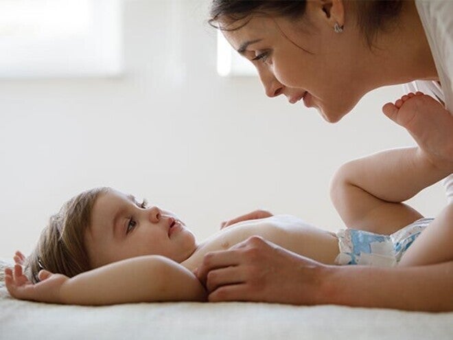 Foto: moeder kijkt liefdevol naar baby op bed, rustige warme sfeer
