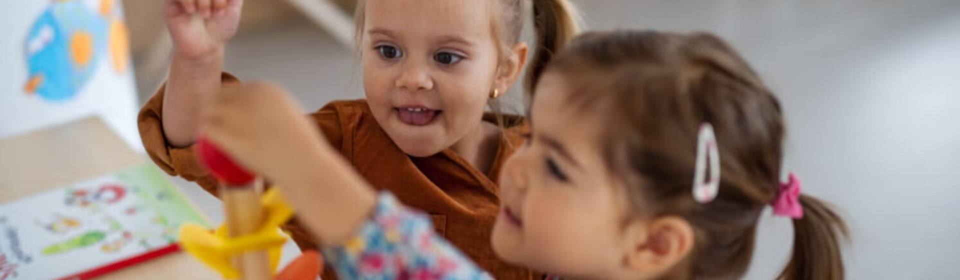 Photo: two smiling toddlers stacking colorful wooden rings in a bright playroom