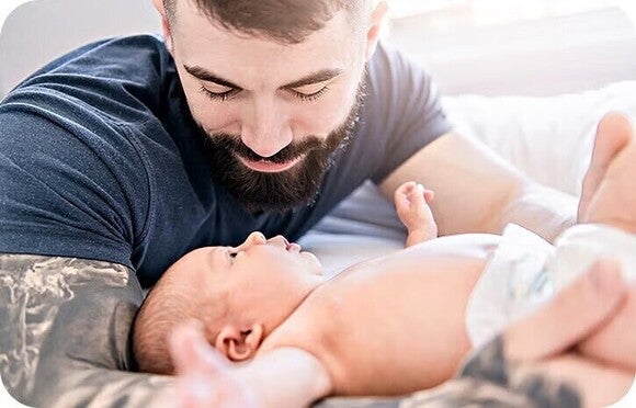 Foto van een glimlachende vader die liefkozend naar zijn pasgeboren baby op bed kijkt